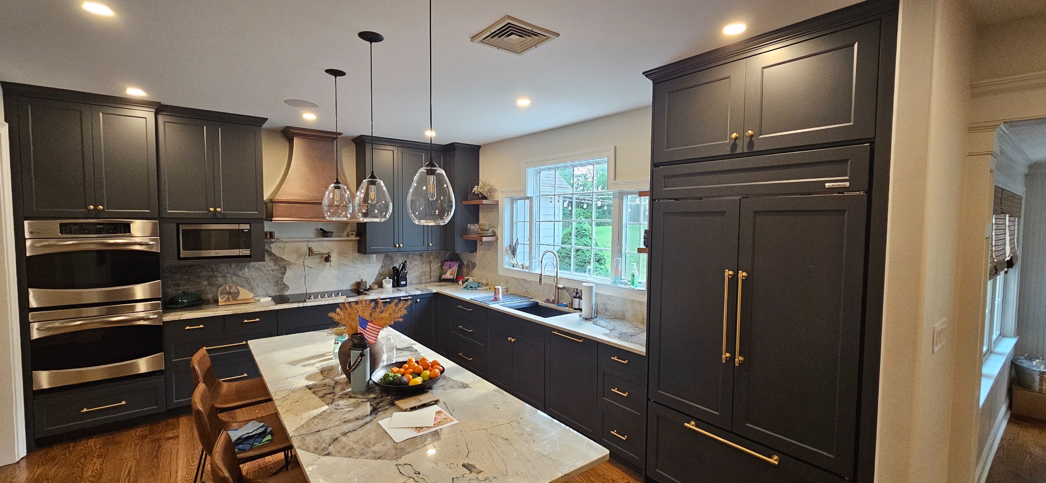 Custom frameless full-overlay kitchen in dark painted cabinetry with brass hardware, stone countertops, a large island and a custom copper range hood, built by Brobst Custom Cabinetry & Design LLC in Perkiomenville, PA